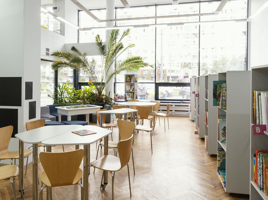 Biblioteca con mobiliario de madera, estanterías blancas y grandes ventanales que llenan el espacio de luz natural.